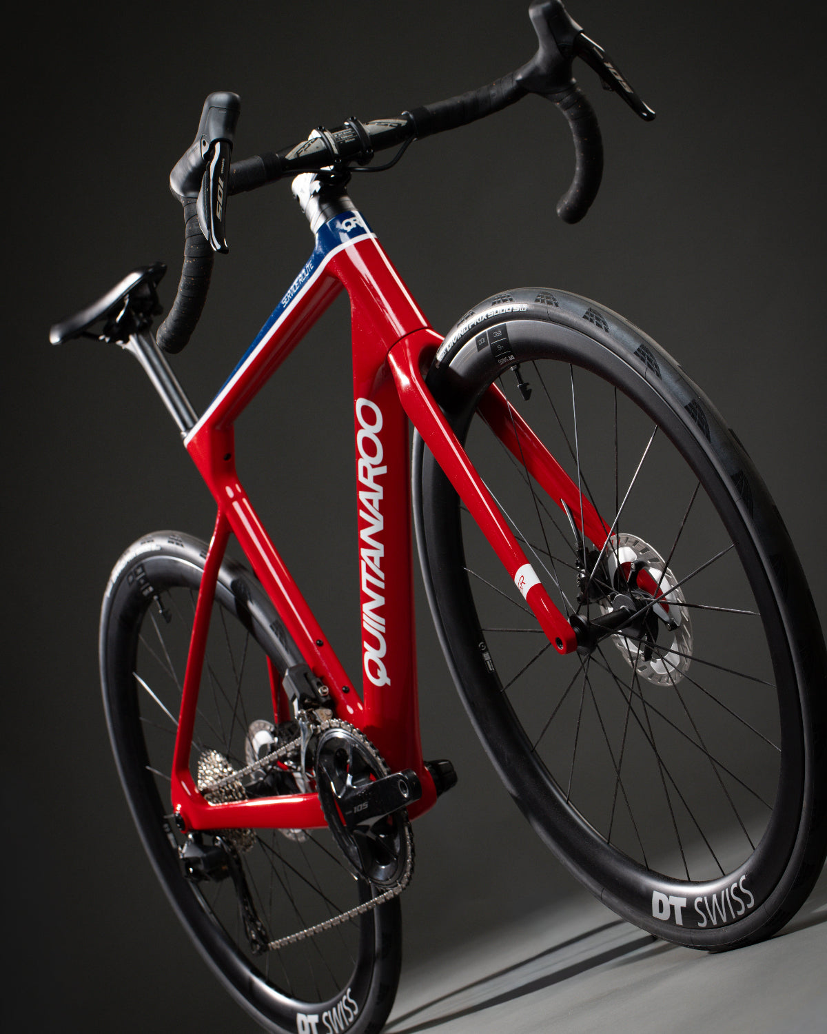 A custom Service Route road bicycle with black components, drop handlebars, and black wheels, photographed on a dark gray studio background.