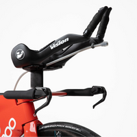 Close-up of a red and black time trial bicycle against a clean white background, showing the handlebar, saddle, and part of the front wheel.