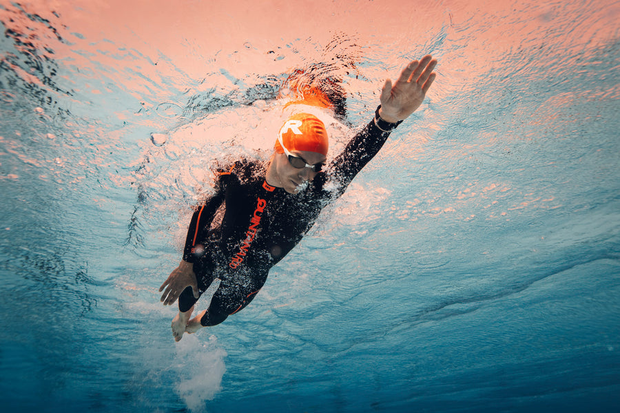 A man wearing a wetsuit, swim cap, and goggles swimming face-down in a pool.