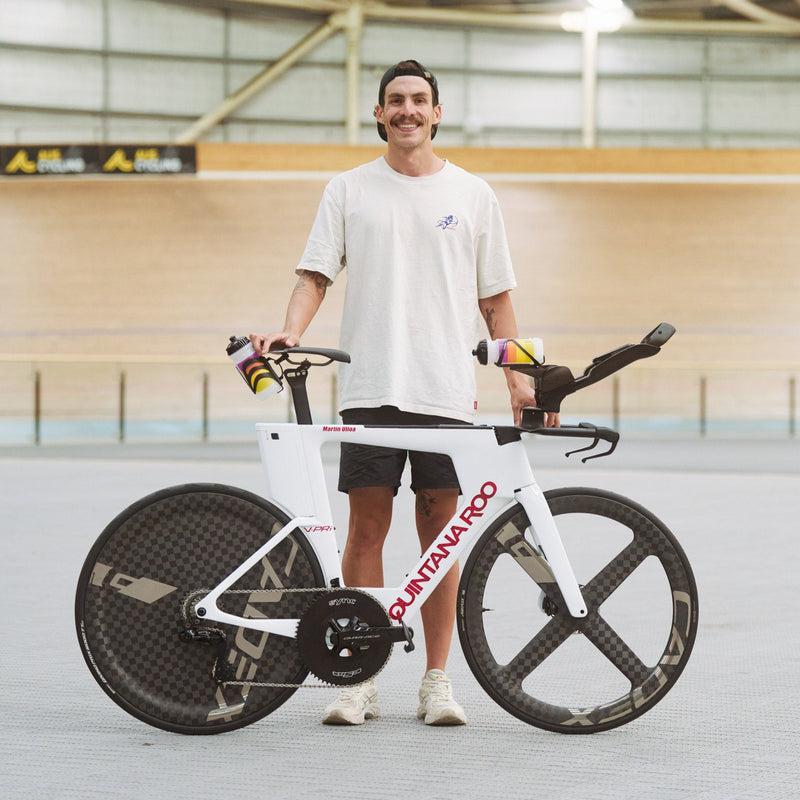 Man holding a white track bike with black wheels in an indoor cycling track.