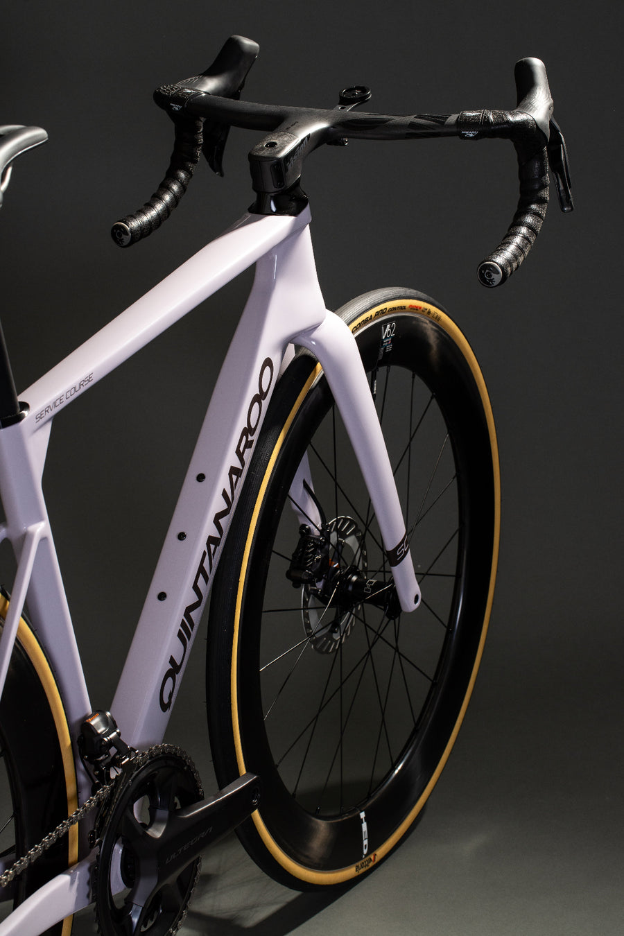 A close-up studio shot of a high-performance road bicycle, showing the white Quintana Roo frame, black drop handlebars with black grips, and deep black carbon wheels with a distinctive yellow sidewall stripe.