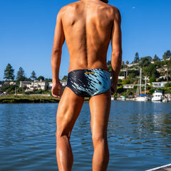 Man in swim trunks standing on a dock by a lake with houses and trees in the background