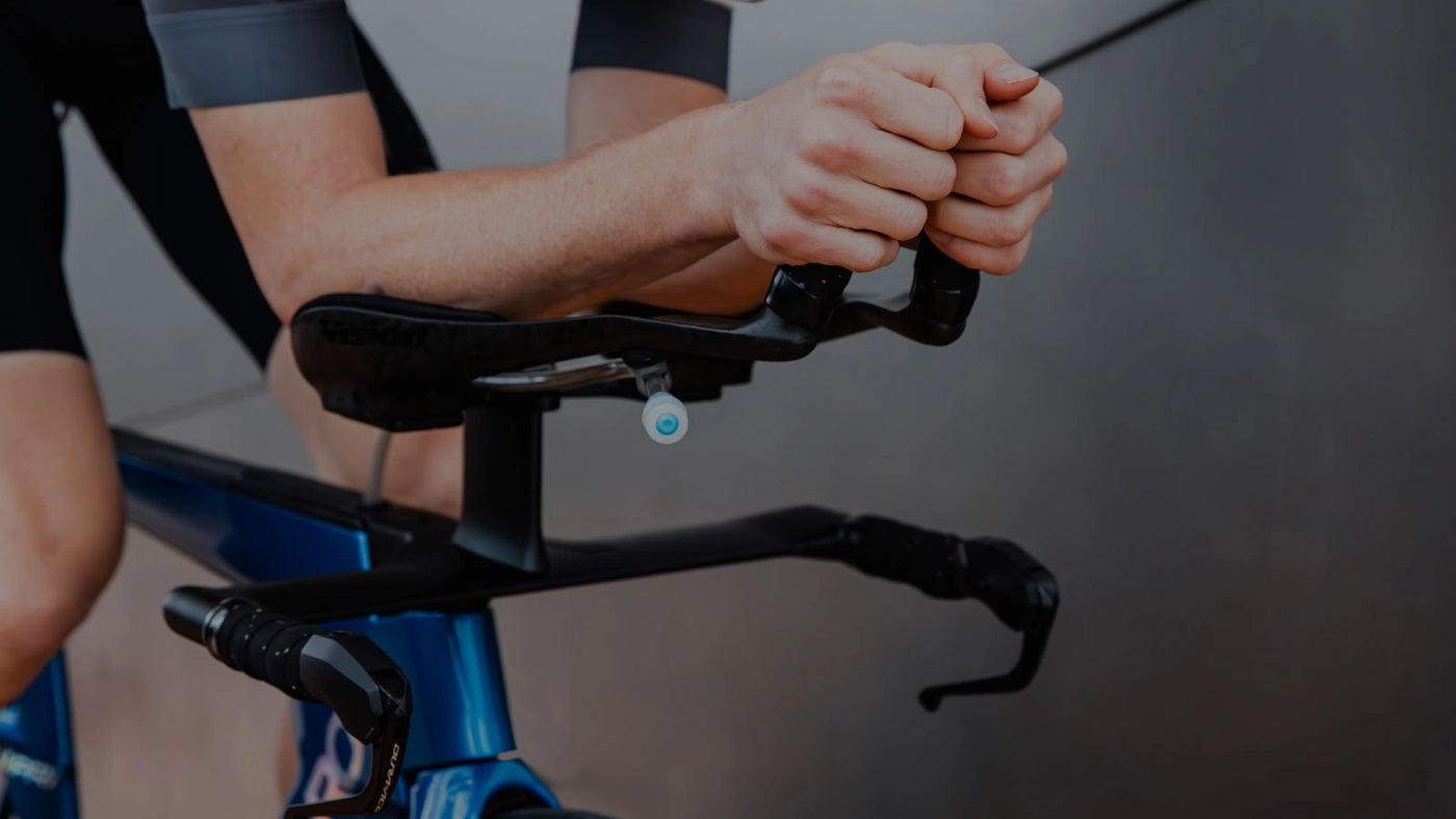 Um close up de um ciclista descansando os braços nas barras de braço de uma bicicleta QR azul.