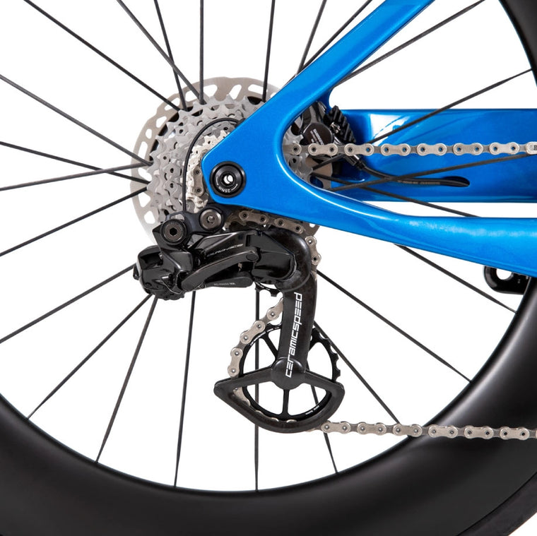 Uma imagem do close up da roda/corrente de uma bicicleta azul de QR em um fundo branco.