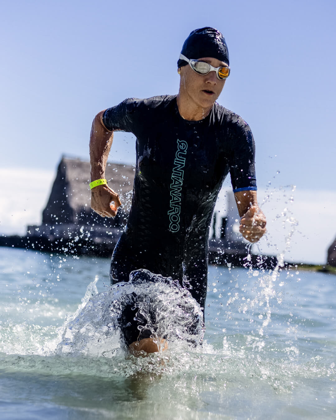 Someone running out of the water wearing a QR wetsuit, swim cap, and goggles